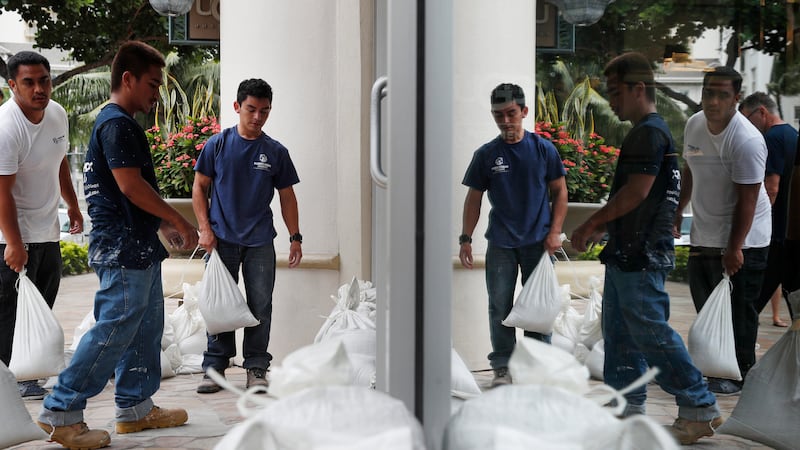 Workers stack sandbags in front of a closed store in preparation for Hurricane Lane, Thursday,...